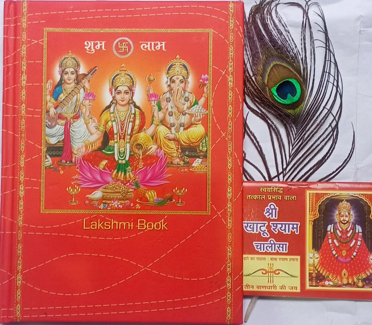 Red book with religious illustrations and a peacock feather on a white background