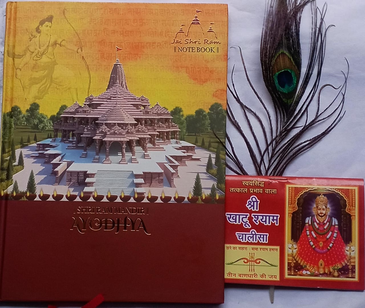 Notebook with temple illustration and peacock feather, alongside another notebook with religious design.