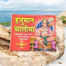 Hindu religious text and illustration on a red background, placed on rocks with a blue sky and ocean in the background.