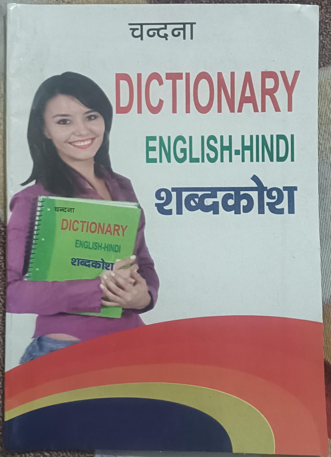 Dictionary cover with a woman holding a green book, featuring text in English and Hindi.