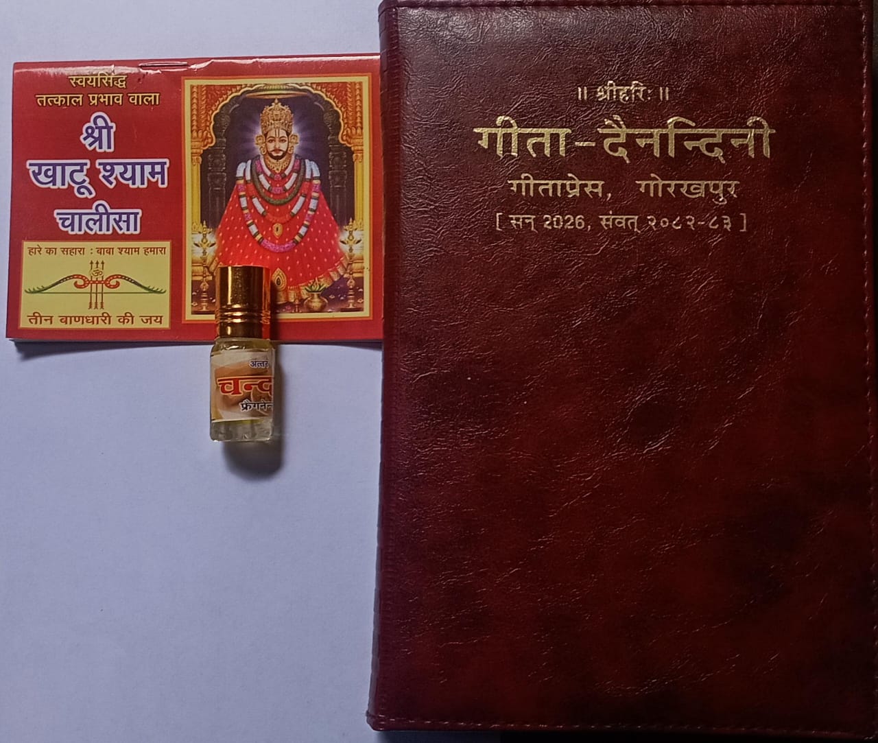 Red leather-bound book with gold text, a small red box with gold design, and a gold bottle on a light purple background.