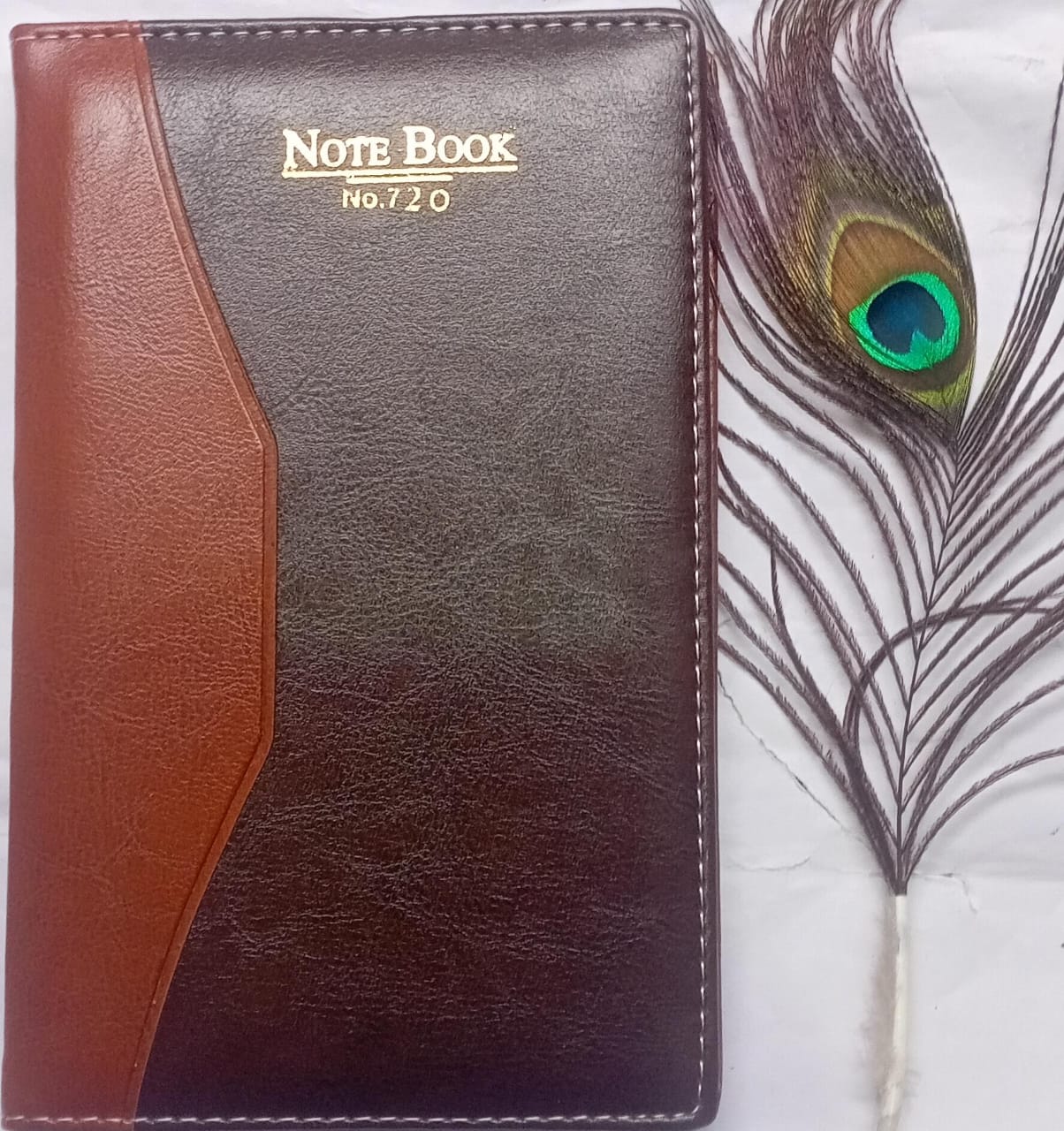 Notebook with brown and black leather cover and peacock feather on white background