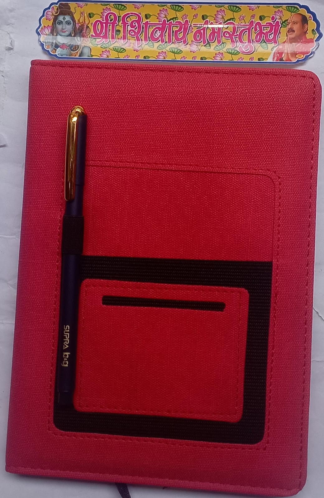 Red notebook with a pen holder and a visible brand logo on a white background