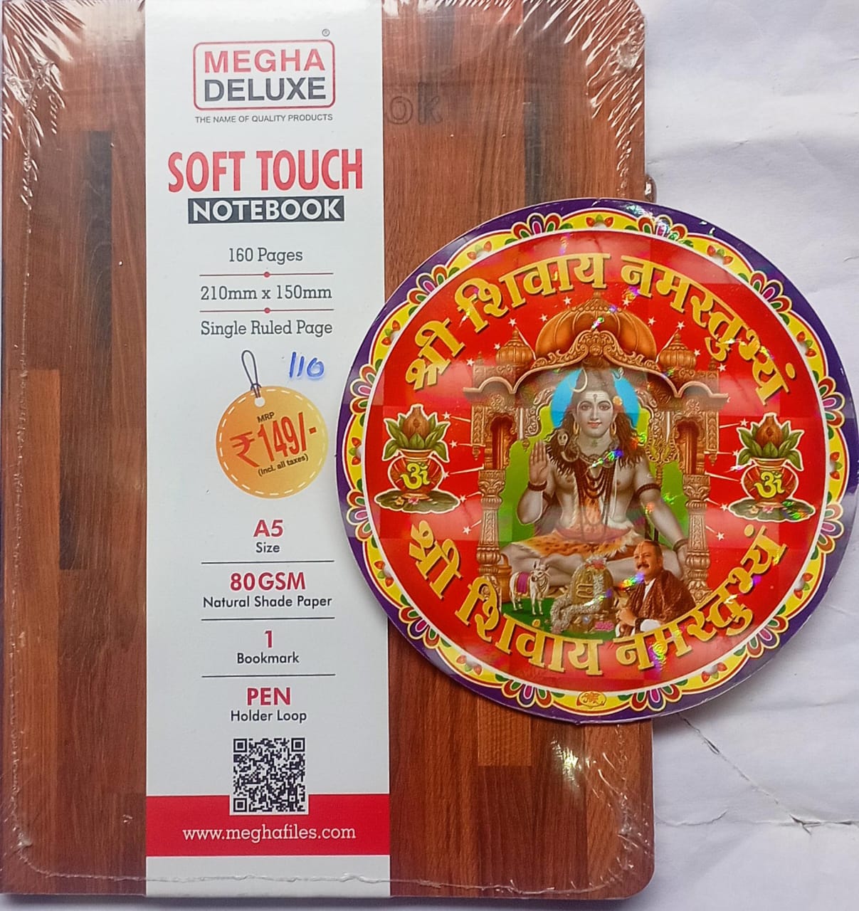 Wooden product with a decorative plate featuring religious iconography and Megha Deluxe notebook packaging.